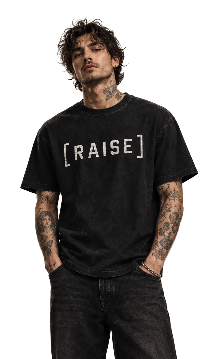 Close-up upper-body shot of the Raise The Stakes tee showing the RAISE graphic, Tilted Spades
